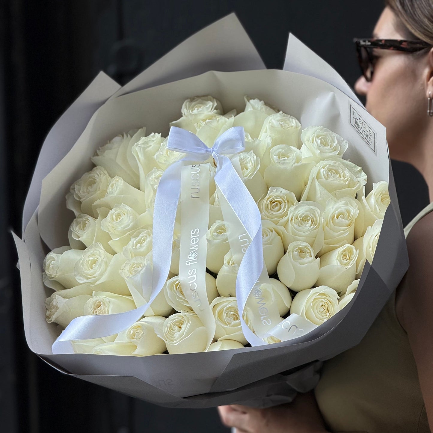 Bouquet of white roses with a white ribbon held by a person against a dark background