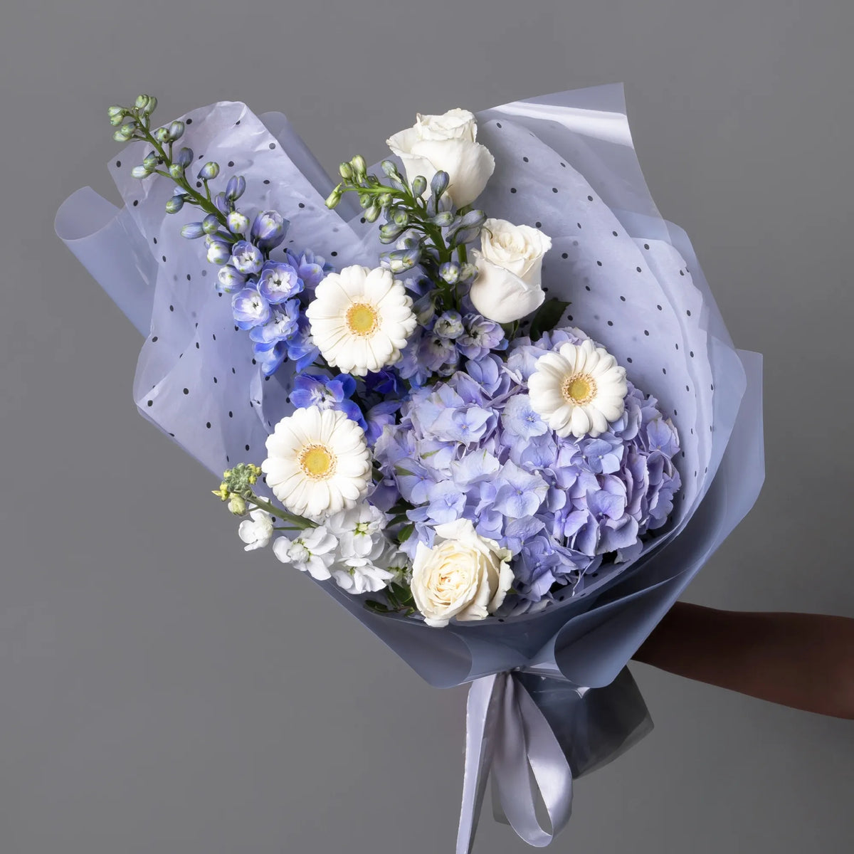 Compliment bouquet with blue hydrangea, roses, gerbera, and light blooms