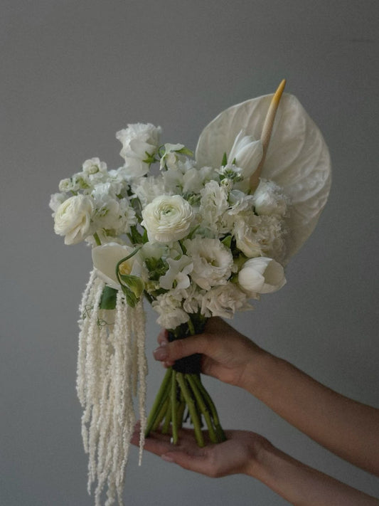 Modern white bridal bouquet with anthurium, ranunculus, tulips, and cascading amaranthus.