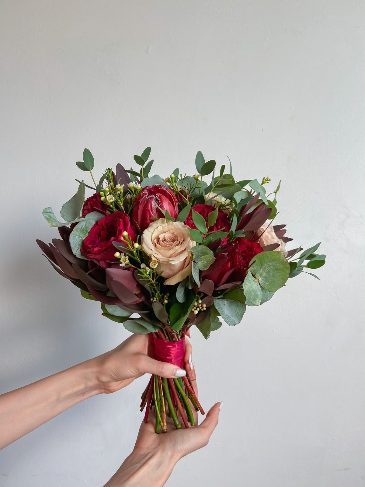Dramatic bridal bouquet with red roses, protea, and textured blooms.