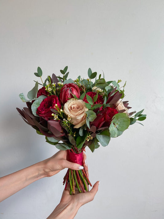 Dramatic bridal bouquet with red roses, protea, and textured blooms.
