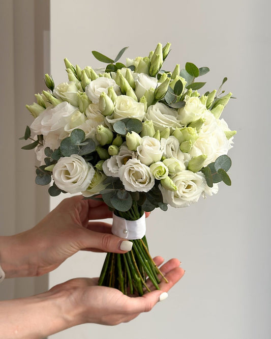White bridal bouquet made of roses, lisianthus, and eucalyptus.