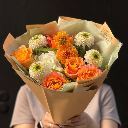 Bouquet of orange and white flowers wrapped in brown paper held by a person against a dark background