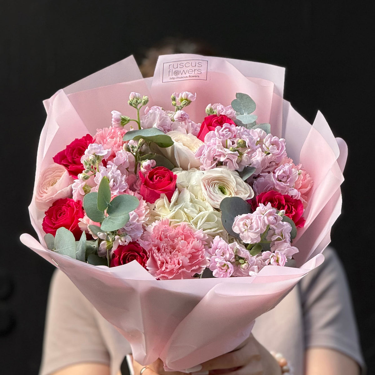 Bouquet of flowers wrapped in pink paper with 'Ruscus Flowers' branding on a black background.