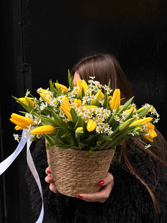 Basket with yellow tulips and white daisies arranged in a woven container