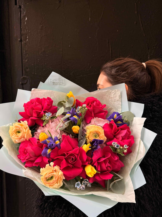 Mixed bouquet with red French roses, irises and ranunculus wrapped in modern paper